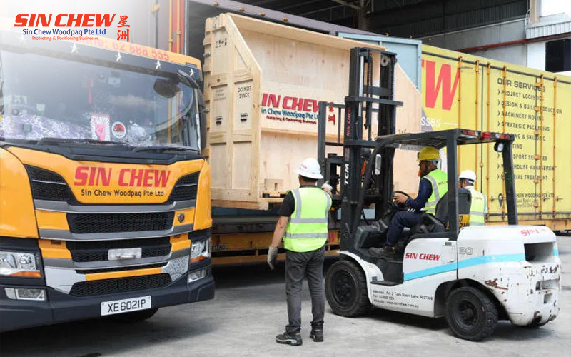 Sin Chew logistics workers using a forklift to load a large wooden crate onto a transport truck.