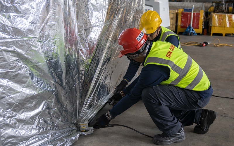 Technicians sealing protective foil wrap during industrial machinery packing.