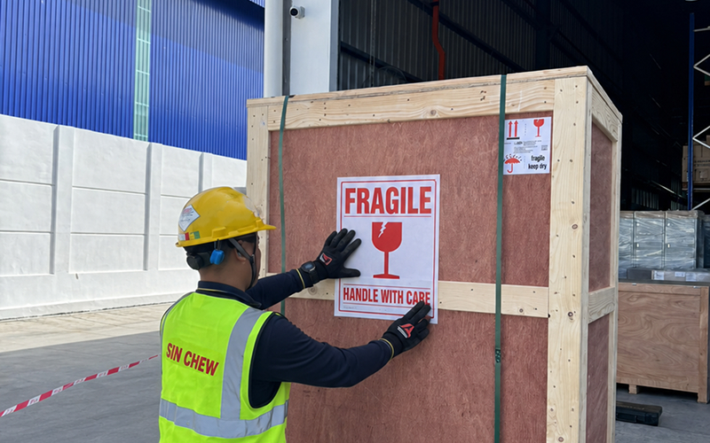 Worker attaching fragile sticker onto wooden cargo shipping crate.